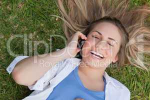 Young laughing girl lying on her back while talking on the phone