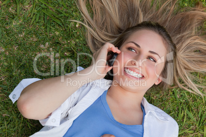 Young smiling woman lying on her back while using her cellphone