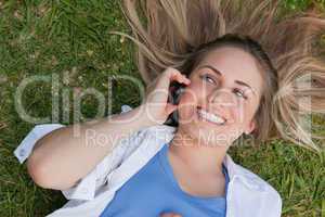 Young smiling woman lying on her back while using her cellphone