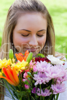 Young blonde girl closing her eyes while smelling a bunch of flo