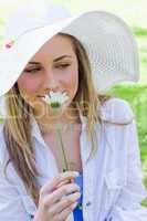 Young peaceful blonde girl smelling a white flower while standin