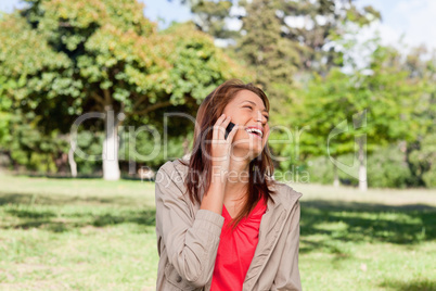 Woman laughing joyfully on a phone while standing in a sunny gra