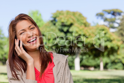 Young woman laughing happily on the phone in a bright park area