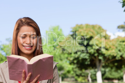 Young woman happily reading a book in a sunny park