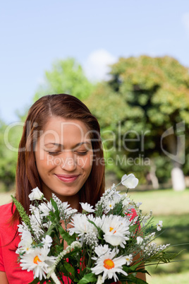 Young woman examining a bunch of flowers while standing in a par