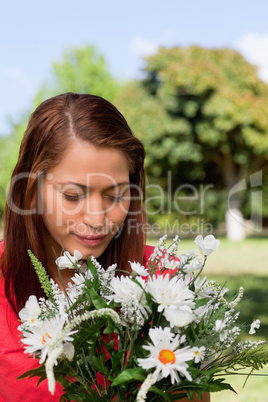 Young woman looking down at a flowers while standing in a park