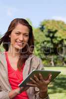Woman smiling and looking ahead while she uses a tablet in a par