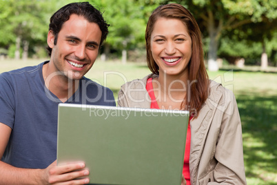 Two smiling friends looking ahead as they hold a tablet