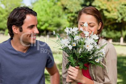 Man smiling as he watches his friend smell a bunch of flowers