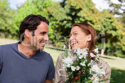 Man watches his friend laughing while holding a bunch of flowers