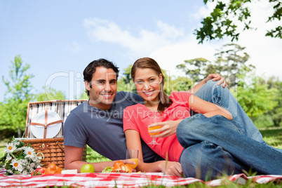 Two friends looking ahead while they hold glasses as they lie on