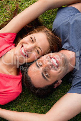 Two friends smiling while lying head to shoulder with an arm out