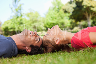 Two smiling friends looking at each other while lying head to he
