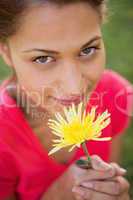 Woman looking upwards while holding a yellow flower