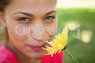 Woman looking upwards while smelling a yellow flower