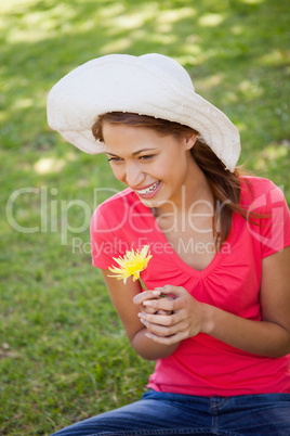 Woman wearing a white hat while holding a yellow flower