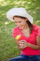 Woman wearing a white hat while holding a yellow flower