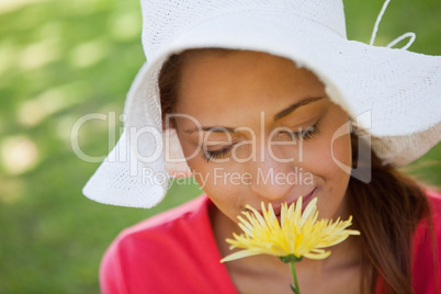 Woman wearing a white hat while smelling a flower with her eyes