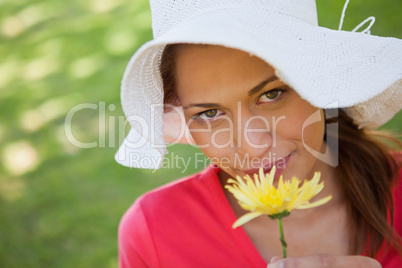 Woman wearing a white hat while smelling a yellow flower