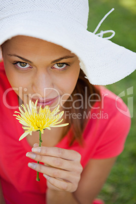 Woman wearing a white hat while smelling a flower while looking