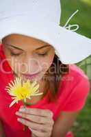Woman wearing a white hat while smelling a flower while looking