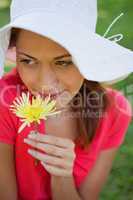 Woman wearing a white hat while smelling a flower while looking