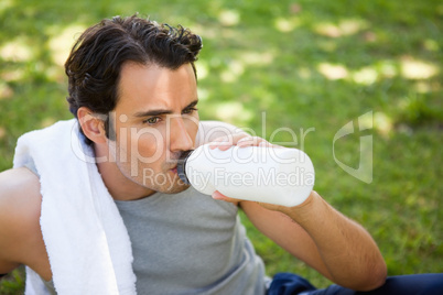 Man with a towel on his shoulder drinking from a sports bottle