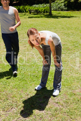 Woman bending over while a man is jogging behind her