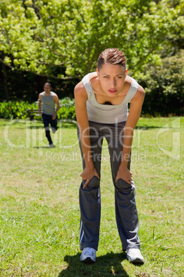 woman bending over while a man is running in the background