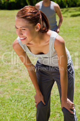 Smiling woman bending over while a man is walkng behind her