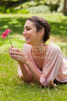 Woman lying on her front laughing while looking at a flower