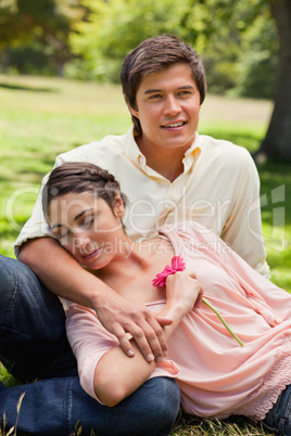 Woman holding a flower while resting against her friend