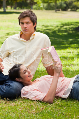 Woman lying against her friend's leg while she is reading