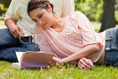 Woman lying down next to her friend while reading a book