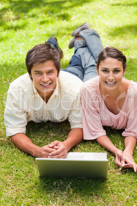 Two friends laughing while looking ahead as they use a laptop