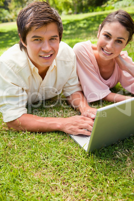 Two friends looking towards the side while using a laptop