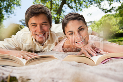 Two friends reading books while lying on a blanket