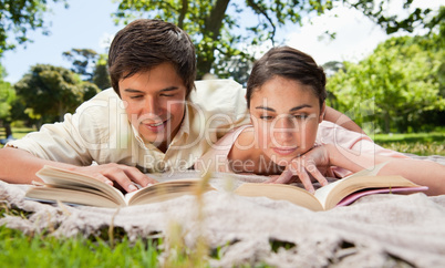 Two friends looking down at books while lying on a blanket
