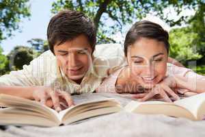 Two friends smiling while reading books as they lie down