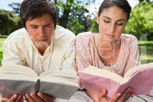 Two friends concentrating on books while lying down