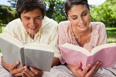 Two friends smiling as they read while lying on a blanket