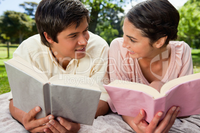 Two friends smiling at each other while reading on a blanket