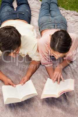 Man and a woman reading while lying on a blanket