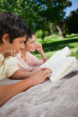 Two friends reading books while lying in a park