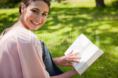 Woman looks to her side while reading a book in the grass