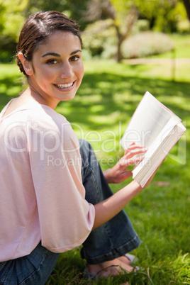 Woman looks to her side while reading a book in a park