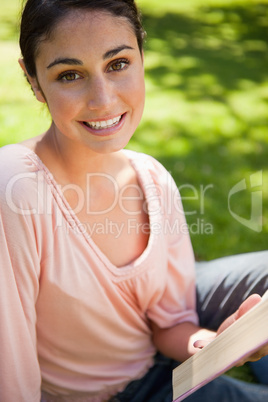 Woman looking ahead as she reads a book while sitting down