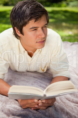 Man looking to his side while reading a book as he lies on a bla