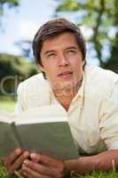 Man looks to the distance while reading a book as he is lying do