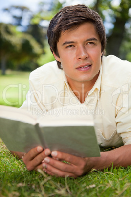 Man looks to the distance while reading a book as he lies on gra